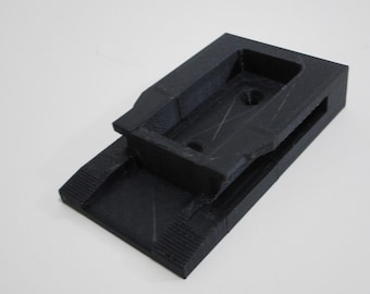 May include: A black plastic 3D printed mount with a rectangular opening and a raised platform.