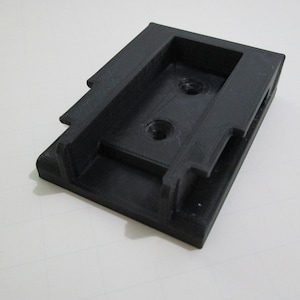 Peut inclure: Pièce en plastique noire imprimée en 3D avec deux trous et une ouverture rectangulaire.