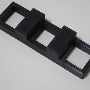 May include: A black plastic 3D printed object with three rectangular openings. The object has two raised sections on the top.