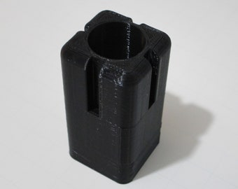 May include: A black 3D printed plastic cylinder with a square base and a circular opening at the top. The cylinder has two vertical slots on one side.