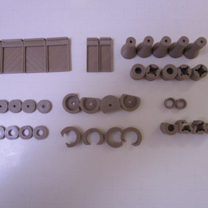 Può includere: Assortimento di pezzi di plastica marroni, tra cui piccoli cerchi, quadrati e altre forme. Questi pezzi sono probabilmente per un modello o un progetto artigianale.