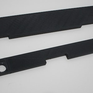 May include: Two black plastic pieces with cutouts and holes. These pieces are likely for a 3D printed project.
