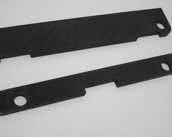 May include: Two black plastic pieces with cutouts and holes. These pieces are likely for a 3D printed project.