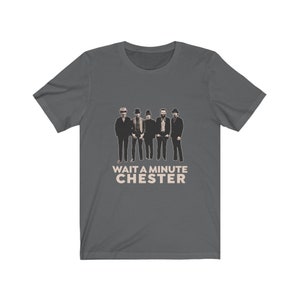 May include: A dark gray t-shirt with a graphic of five men in hats and the text "WAIT A MINUTE CHESTER" in a light brown color.