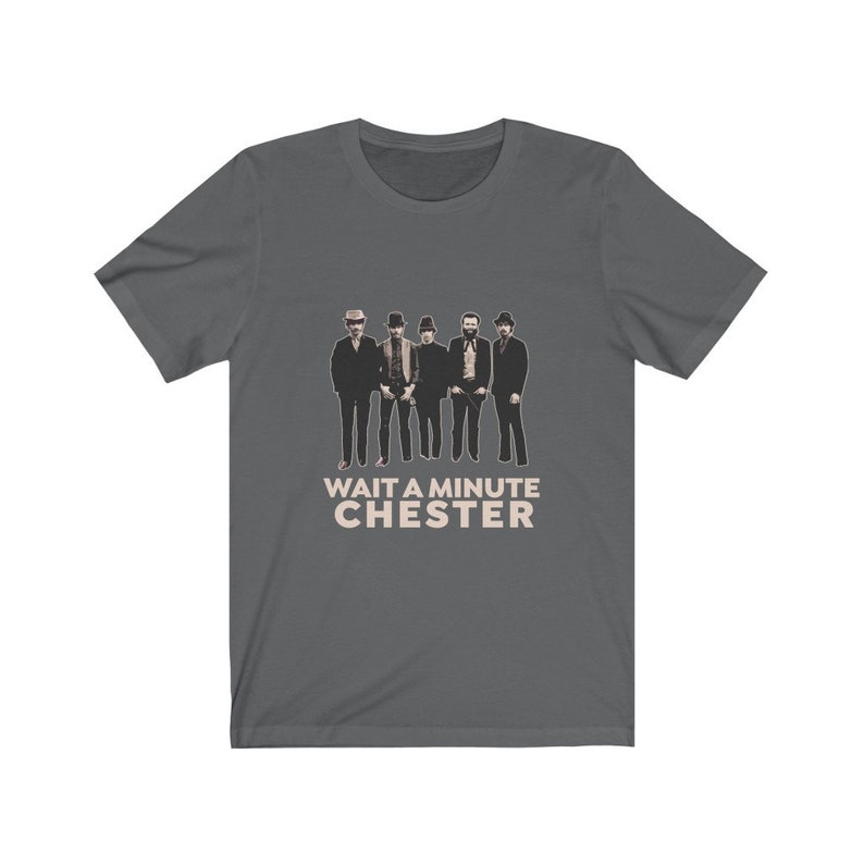 May include: A dark gray t-shirt with a graphic of five men in hats and the text "WAIT A MINUTE CHESTER" in a light brown color.