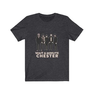 May include: A dark heather grey t-shirt with a black and white image of a band with the text "WAIT A MINUTE CHESTER" printed on the front.