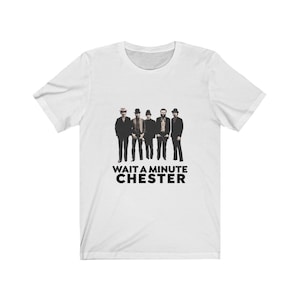 May include: White t-shirt with a black and white image of five men wearing hats and suits. The text "WAIT A MINUTE CHESTER" is printed below the image.