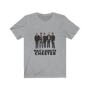 May include: A gray t-shirt with a black and white image of a band of five men wearing hats and suits. The text "WAIT A MINUTE CHESTER" is printed below the image.