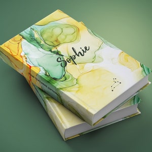 May include: Two hardcover books stacked on top of each other. The covers feature a colorful abstract design in yellow, green, and orange. The name "Sophie" is written in cursive on the top book. A constellation is printed on the bottom right corner.