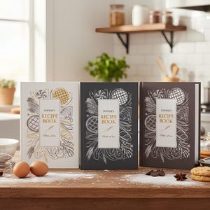 May include: Three hardcover recipe books titled Sophie's Recipe Book, Made with love, displayed in white, black, and dark brown. Each cover features intricate white and gold illustrations of wheat, baked goods, and kitchen ingredients.