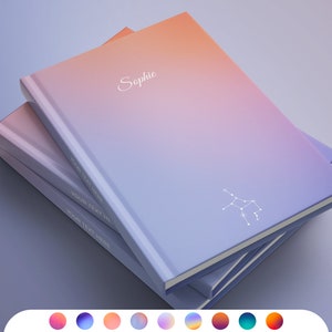 May include: A stack of three notebooks with a gradient color design. The top notebook has the name "Sophie" printed on the front and a constellation design. The notebooks are in shades of purple, pink, and orange.