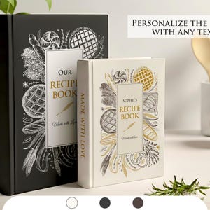 Puede incluir: Dos libros de recetas, uno negro y otro crema, con cubiertas ilustradas con diseños relacionados con la comida. El libro negro dice "Our Recipe Book" y el libro crema dice "Sophie's Recipe Book". Ambos libros tienen el texto "Made with Love".