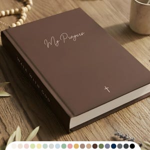 Könnte beinhalten: Ein braunes Notizbuch mit den Worten "My Prayers" in Schreibschrift und einem kleinen Kreuzsymbol. Auf dem Buchrücken steht "Walk With God". Das Notizbuch liegt auf einer Holzoberfläche mit einem Rosenkranz, einem Kreuz und einer kleinen Tasse.
