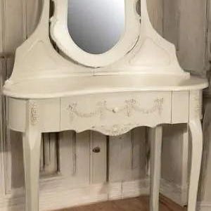 May include: A white vanity table with a carved design and a tilting mirror. The table has a single drawer and a curved top.