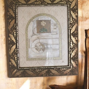 May include: A framed artwork with a gold and brown frame. The artwork is a collage of paper with a floral design in the centre. The frame has a decorative pattern of leaves.