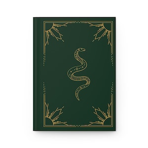 Puede incluir: Una cubierta de diario verde oscuro con un diseño de serpiente dorada y patrones de rayos de sol. La serpiente está enroscada y tiene un diseño estilizado con puntos y líneas.