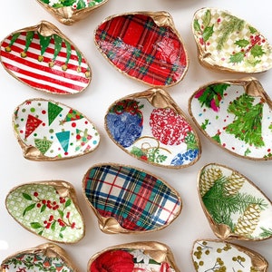 May include: A collection of decorative seashell dishes with gold-painted edges. Each shell is uniquely decorated with festive holiday patterns, including holly, plaid, and Christmas tree designs. These shells are perfect for holding small items or as decorative accents.
