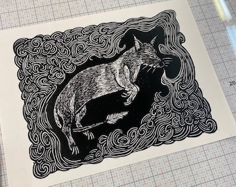 May include: Black and white linocut print of a fox leaping through a swirling, stylized cloud design. The fox is detailed with textured shading, and a feather is in the background. The artwork is on a white background.