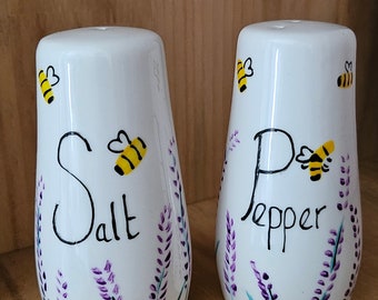 Puede incluir: Salero y pimentero de cerámica blanca con diseños de lavanda y abejas. El salero dice "Salt" y el pimentero dice "Pepper".