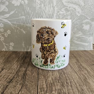 May include: White ceramic mug decorated with a brown dog wearing a yellow collar, with bees and paw prints. The dog stands on green grass. A delightful design for dog enthusiasts.