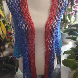 May include: A crocheted shawl with a gradient of blue, purple, and red colors. The shawl is made with a delicate openwork stitch and has a fringed edge.
