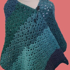 May include: A crocheted shawl in shades of blue and green. The shawl is made with a simple stitch pattern and has a fringed edge.