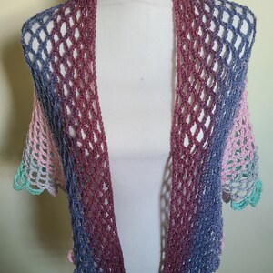 May include: A crocheted shawl with a gradient of pink, purple, and blue colors. The shawl is made with a delicate openwork stitch and has a scalloped edge.