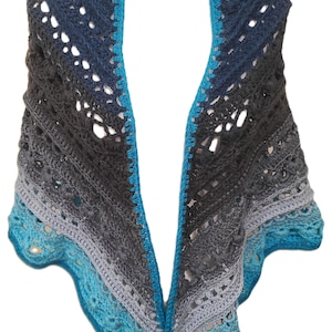 May include: A crocheted shawl with a gradient of blue, gray, and black colors. The shawl has a lacy pattern and a blue border.