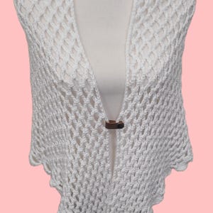 May include: White crochet shawl with a decorative wooden button closure. The shawl is made of a delicate, open-weave fabric.