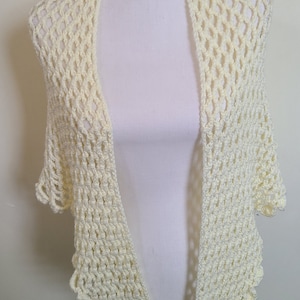 May include: A delicate, crocheted shawl in a pale yellow color. The shawl has a lacy, openwork design and a scalloped edge.