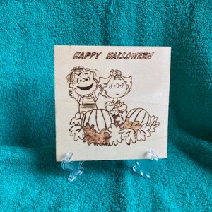 May include: A wooden sign with the text "Happy Halloween" and a cartoon image of two children holding pumpkins. The sign is on a teal blue surface.