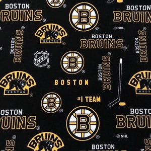 May include: Black fabric with a repeating pattern of the Boston Bruins logo. The logo features a bear, the words "Boston Bruins", and the NHL logo. The fabric also includes the words "#1 Team" and "Boston Bruins" in a gold color.