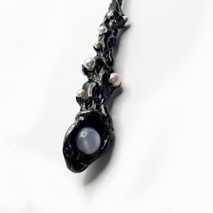 May include: A black wand with a textured surface, adorned with various sized pearls in white, pink, and silver. The wand's handle features a large, pale blue orb. A unique, handcrafted item.