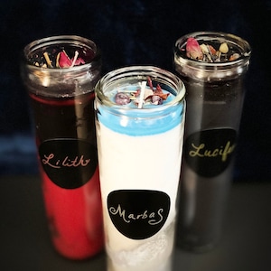 May include: Three glass candle jars with black labels and white text. The candles are red, white, and black. The labels read "Lilith", "Marbas", and "Lucifer".