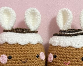 Può includere: Due giocattoli di peluche all'uncinetto a forma di pan di zenzero con glassa bianca e glassa marrone. I giocattoli hanno orecchie di coniglio bianche e guance rosa.