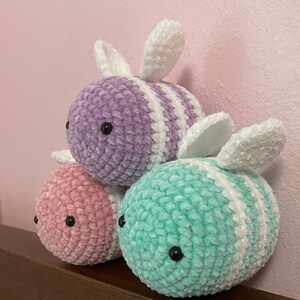 Pu&ograve; includere: Tre peluche di api all'uncinetto in rosa, viola e turchese. Ogni ape ha strisce bianche e ali bianche.