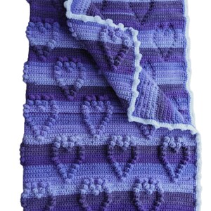 May include: A purple and blue crocheted baby blanket with a white crocheted border. The blanket is folded in half and has a heart pattern.