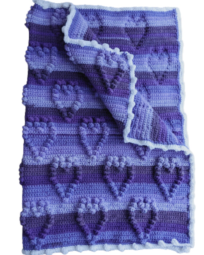 May include: A purple and blue crocheted baby blanket with a white crocheted border. The blanket is folded in half and has a heart pattern.