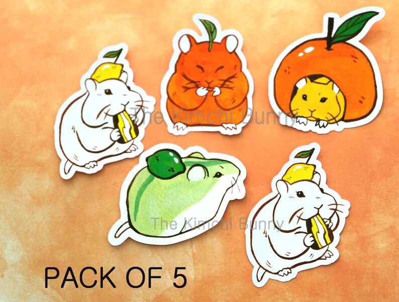 May include: A set of five stickers featuring cute cartoon hamsters wearing fruit hats. The hamsters are eating fruit and are in various poses. The stickers are printed on white paper and have a glossy finish. The text "PACK OF 5" is printed at the bottom of the image.