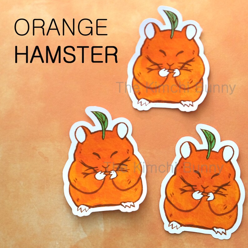 May include: Three orange hamster stickers with a green leaf on top. The hamsters are holding their paws in front of their faces. The stickers are on a peach-colored background.