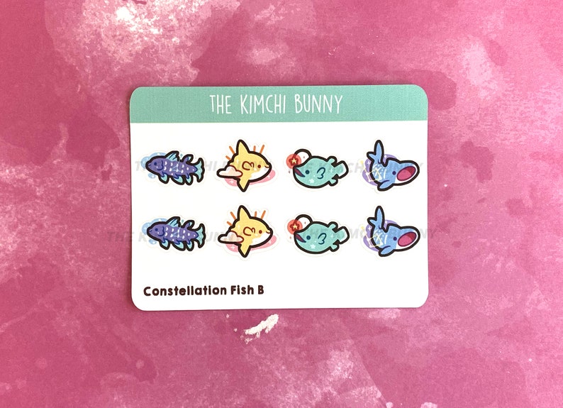 May include: A sheet of stickers featuring a constellation fish design. The stickers are blue, yellow, and green. The text "The Kimchi Bunny" and "Constellation Fish B" are printed on the sheet.