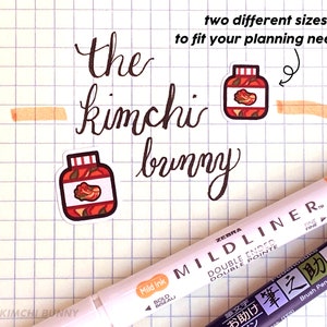 May include: Two different sizes of stickers featuring a jar of kimchi. The stickers are on a sheet of graph paper with a black and white Zebra Mildliner pen and a black brush pen with Japanese text.