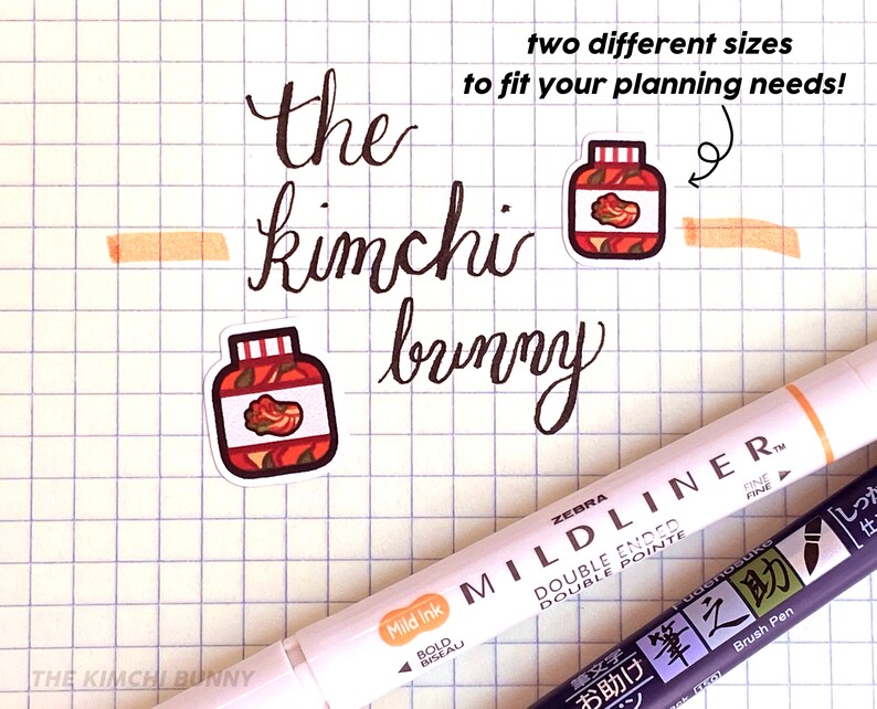 May include: Two different sizes of stickers featuring a jar of kimchi. The stickers are on a sheet of graph paper with a black and white Zebra Mildliner pen and a black brush pen with Japanese text.