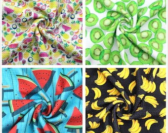 May include: Four fabric swatches with different fruit patterns. The top left swatch features a white background with a variety of colorful fruits, including pineapples, watermelon, and strawberries. The top right swatch features a white background with green kiwi slices. The bottom left swatch features a blue background with red watermelon slices. The bottom right swatch features a black background with yellow bananas.