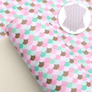 May include: Pink and green mermaid scale fabric with gold glitter accents. The fabric is rolled up and has a white background.