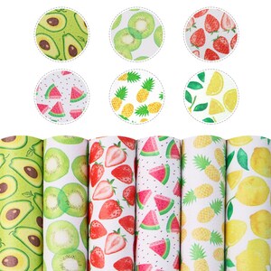 May include: Six rolls of white fabric with different fruit patterns. The patterns include avocado, kiwi, strawberries, watermelon, pineapple, and lemon.