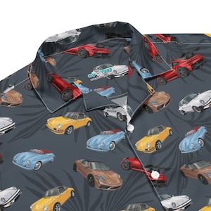 May include: A dark blue button-up shirt with a tropical leaf pattern and a repeating image of various vintage and modern Porsche cars. The shirt has a white collar and a single button closure.