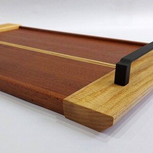 May include: A rectangular wooden serving tray with two black metal handles. The tray is made of two different types of wood, one light and one dark.