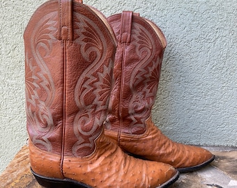 May include: A pair of brown leather cowboy boots with ostrich skin detailing. The boots have a pointed toe and a traditional cowboy boot design.