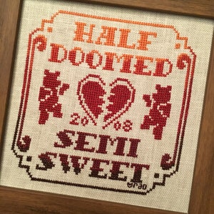 Peut inclure: Broderie au point de croix avec un dégradé de rouge, orange et jaune. Le motif représente deux ours, un cœur brisé et le texte "Half Doomed, Semi Sweet".